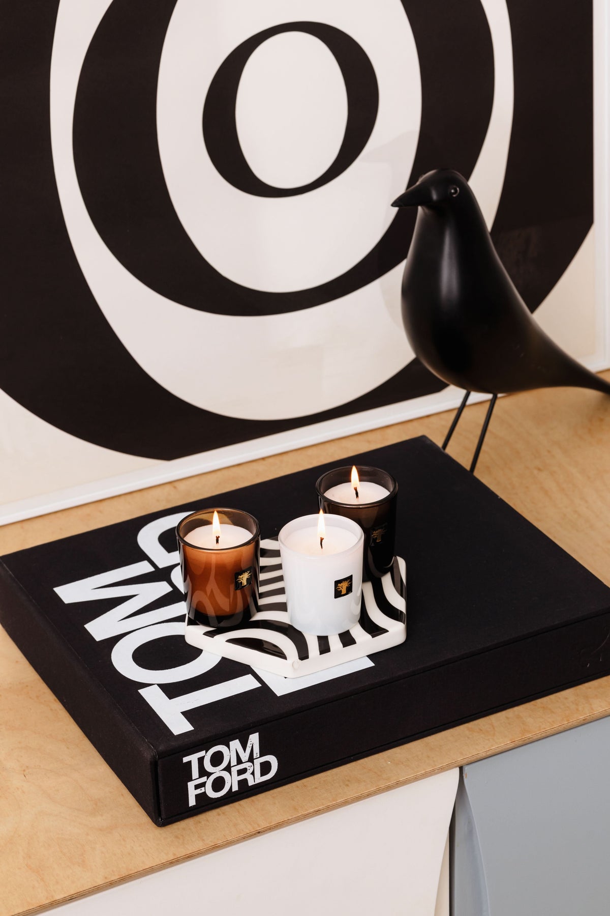 Three lit travel candles in colored glass cups on a black branded tray
