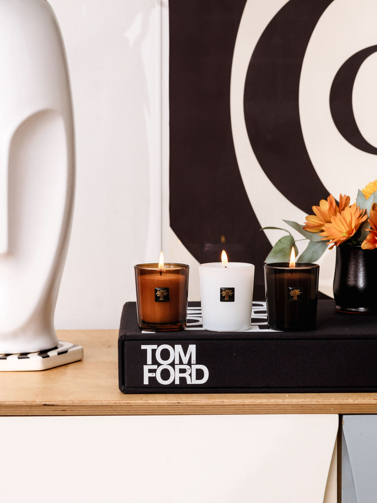Three lit travel candles in brown, white, and dark glass cups on a black tray