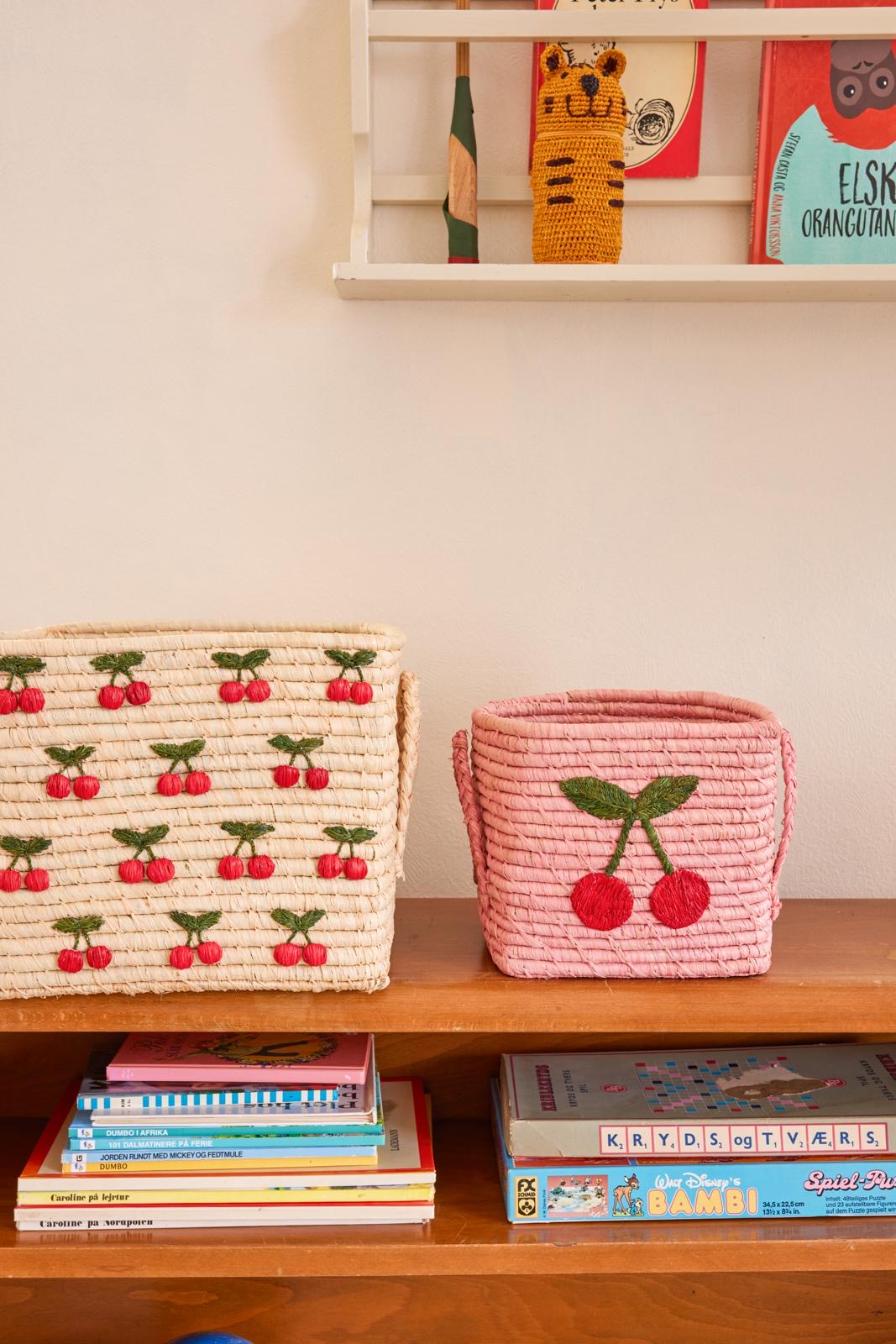 Pink square raffia basket with cherry graphic on a wooden shelf