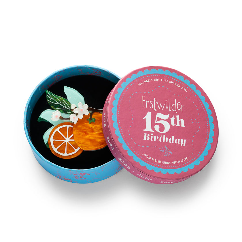 Erstwilder orange fruit brooch inside blue and pink round birthday gift tin