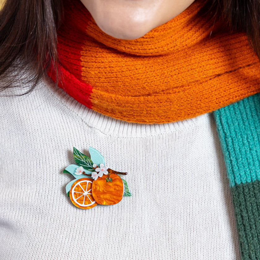Orange fruit enamel brooch pinned on white sweater with orange scarf collar