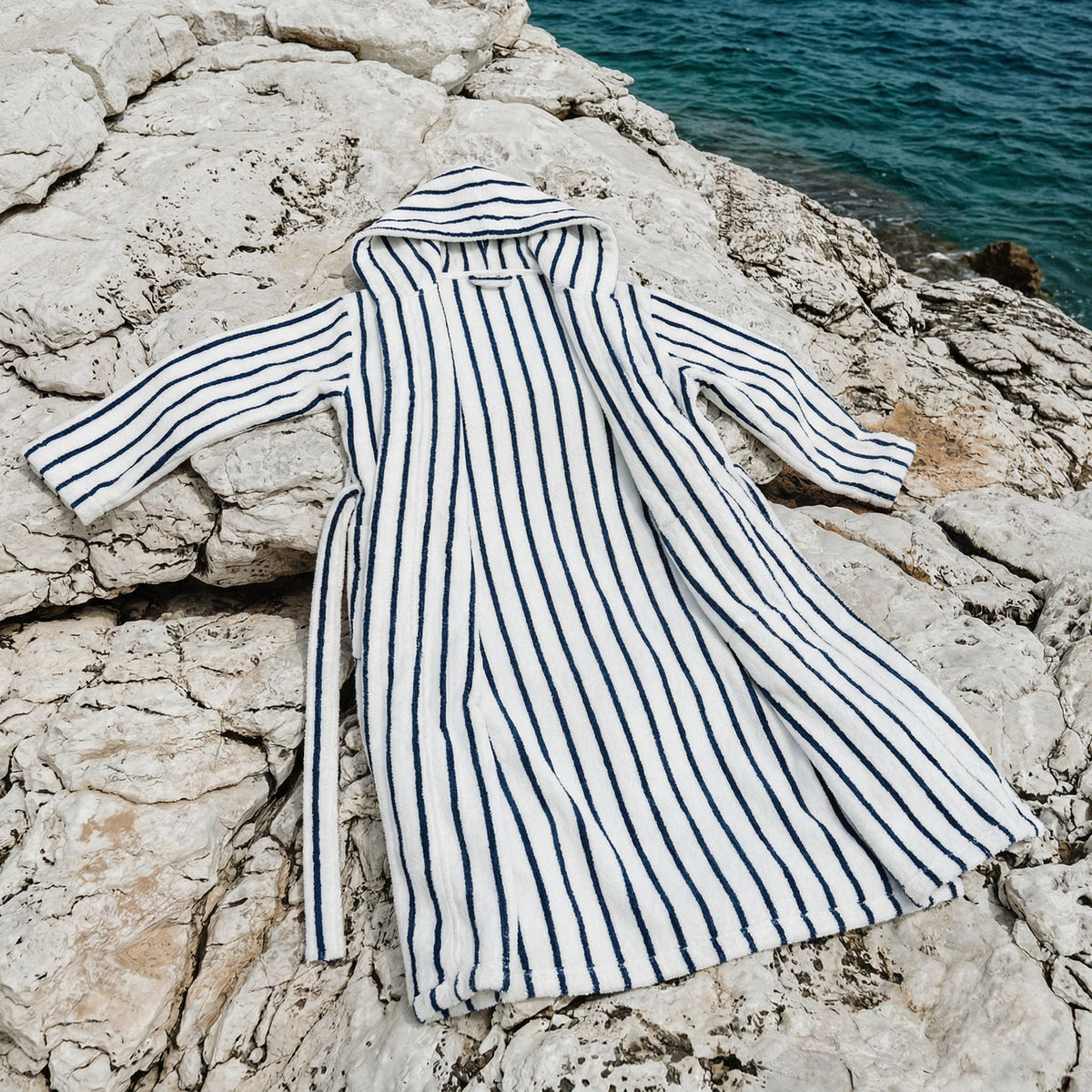 Striped cotton bathrobe with hood and long sleeves laid flat, white with navy vertical stripes