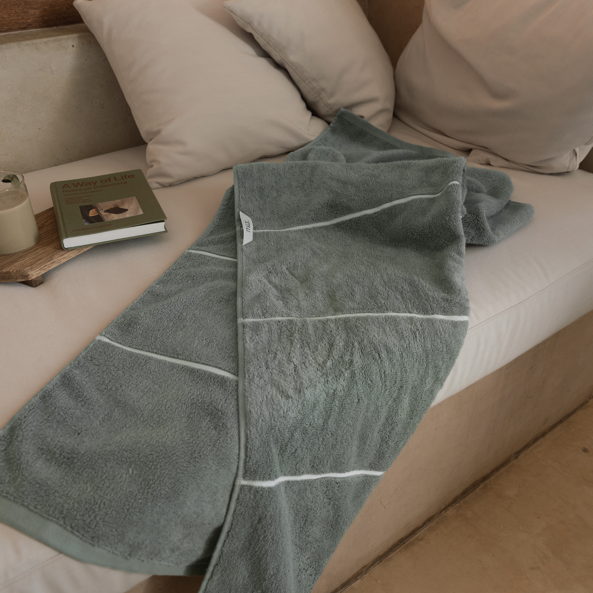 Sage-green cotton towels with white stripe bands, folded on sofa arm