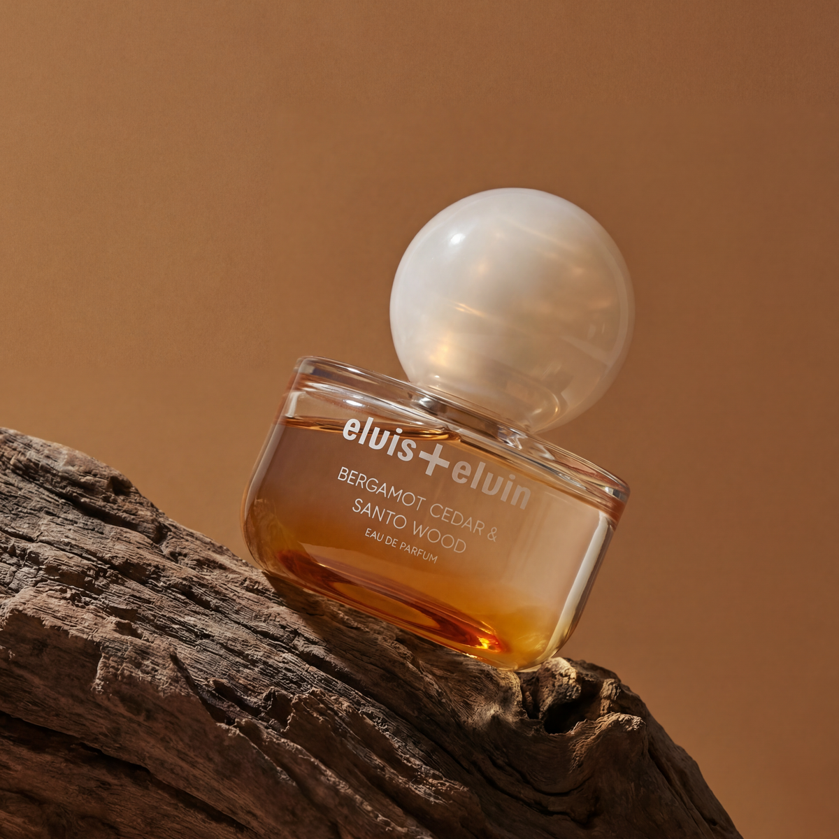 Eau de parfum bottle with amber liquid and clear globe cap on textured wood
