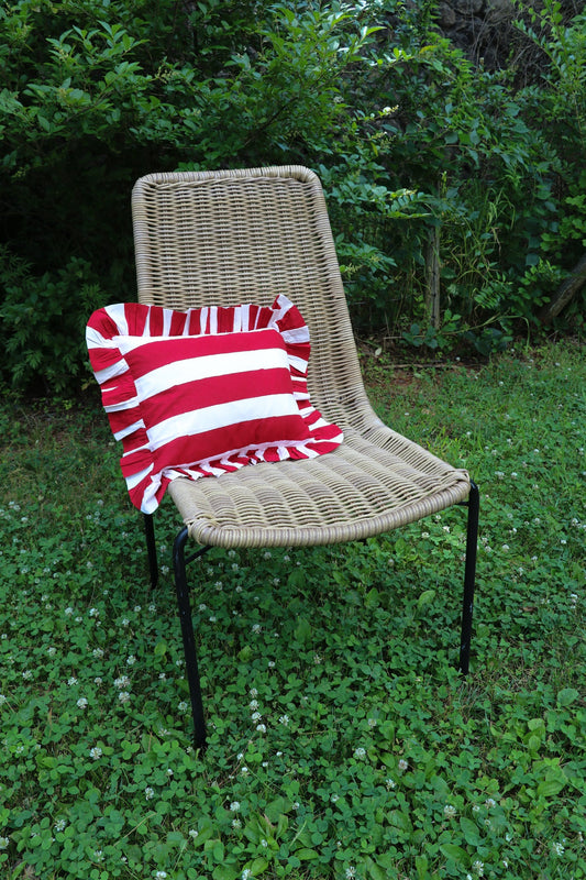 Red and white striped throw pillow with ruffled edges, shown on a woven chair