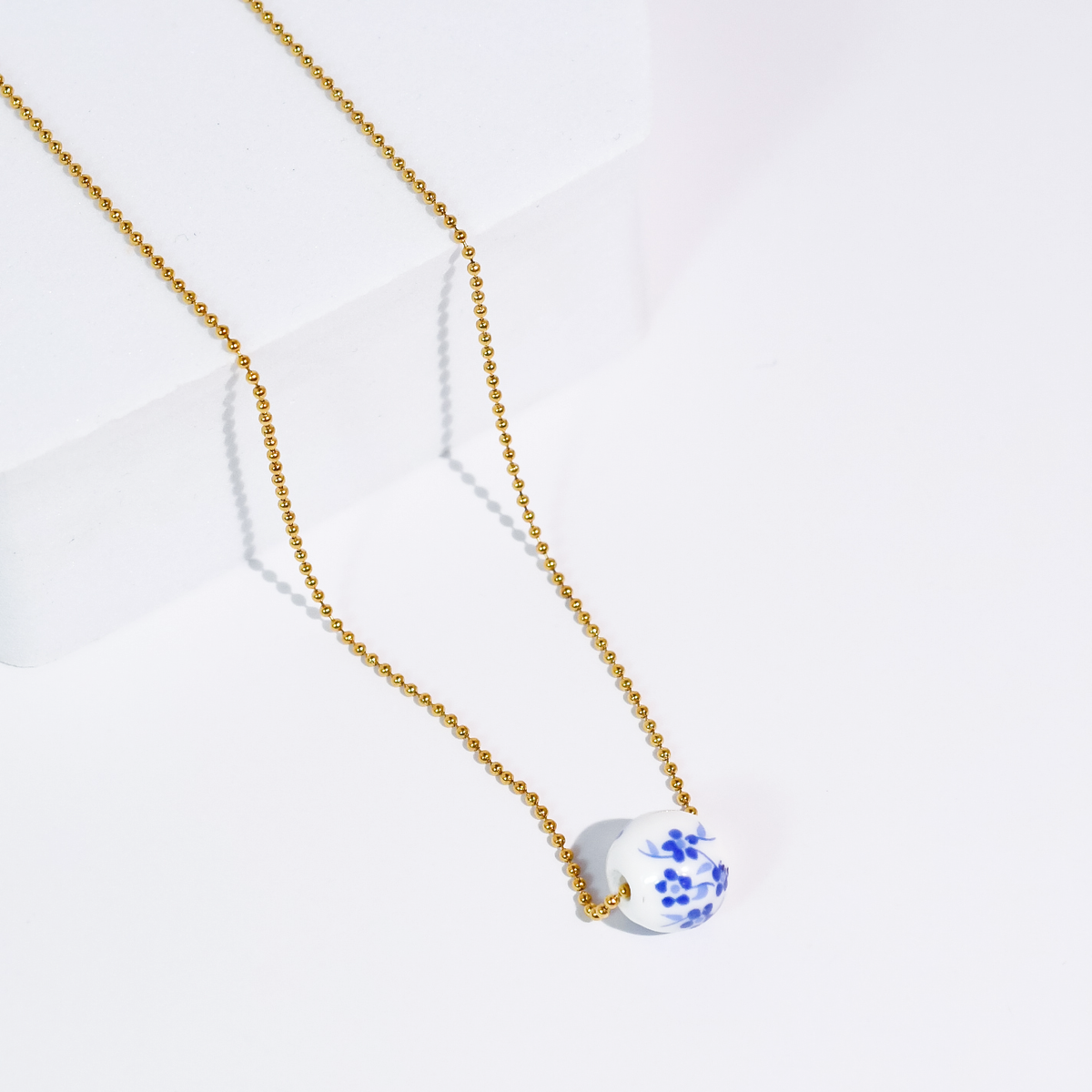 Gold bead necklace with a round blue-and-white floral pendant charm.