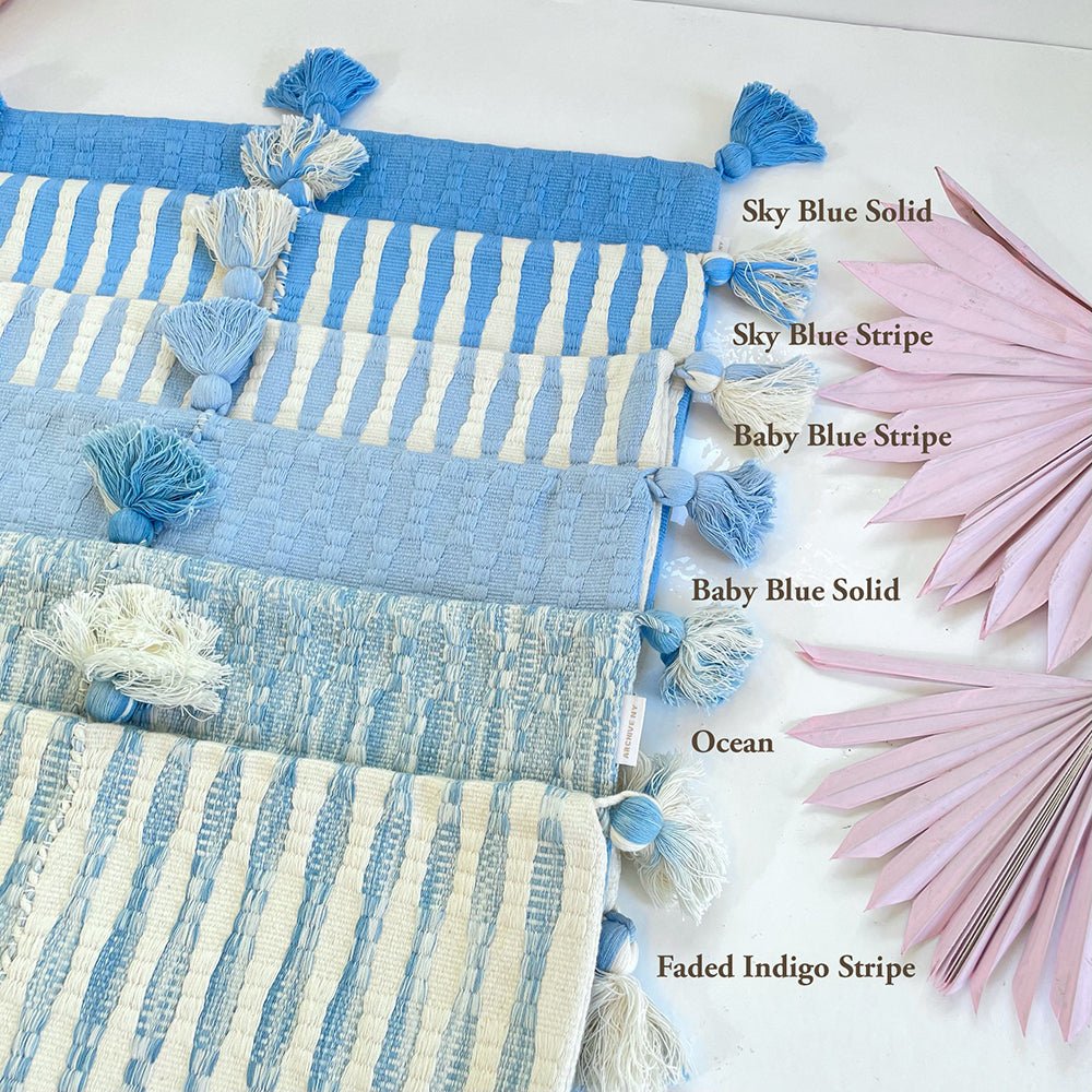 Stack of blue striped and solid pillows with pom tassels, shown as a group