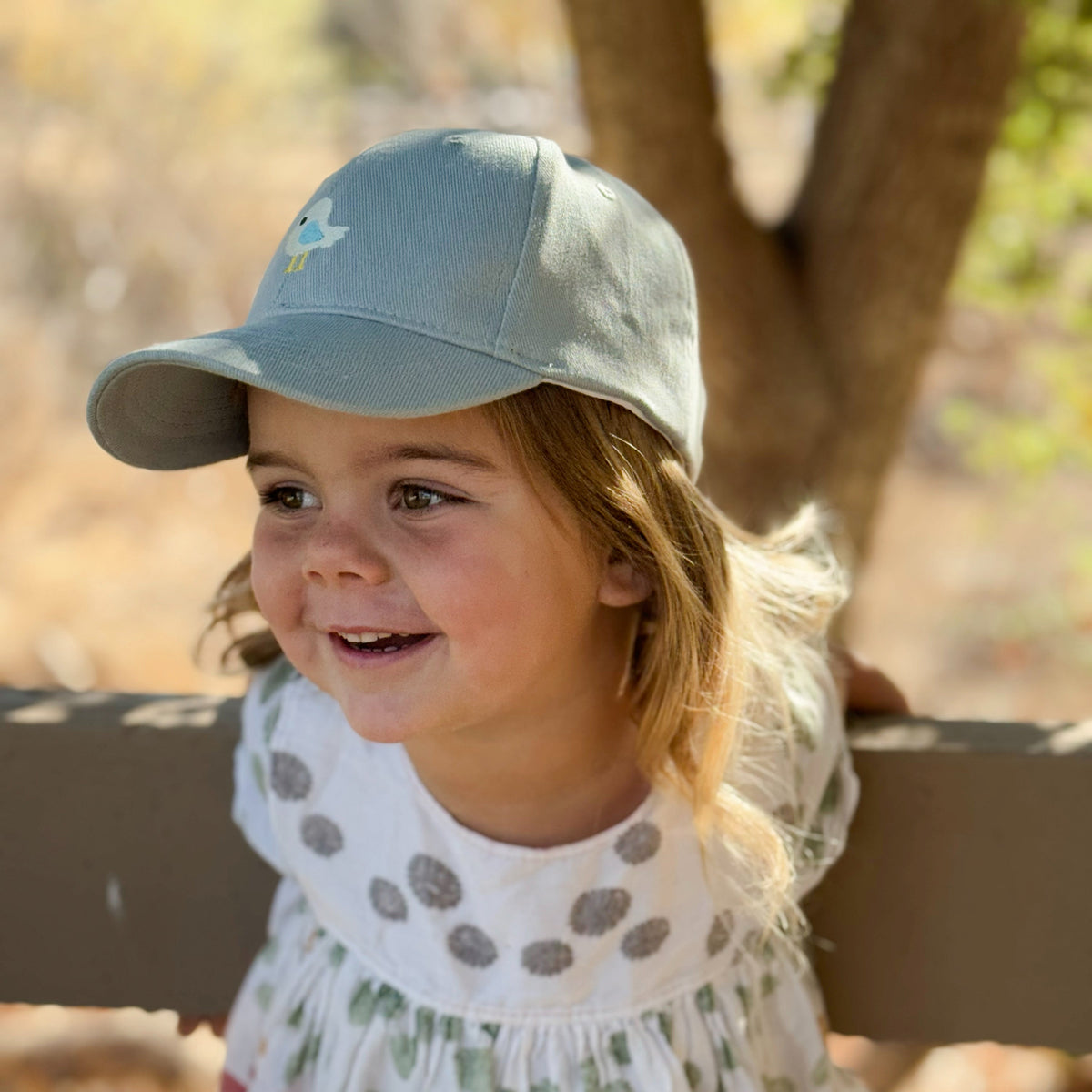 Pale blue children's baseball cap with embroidered bird patch, shown worn by a child