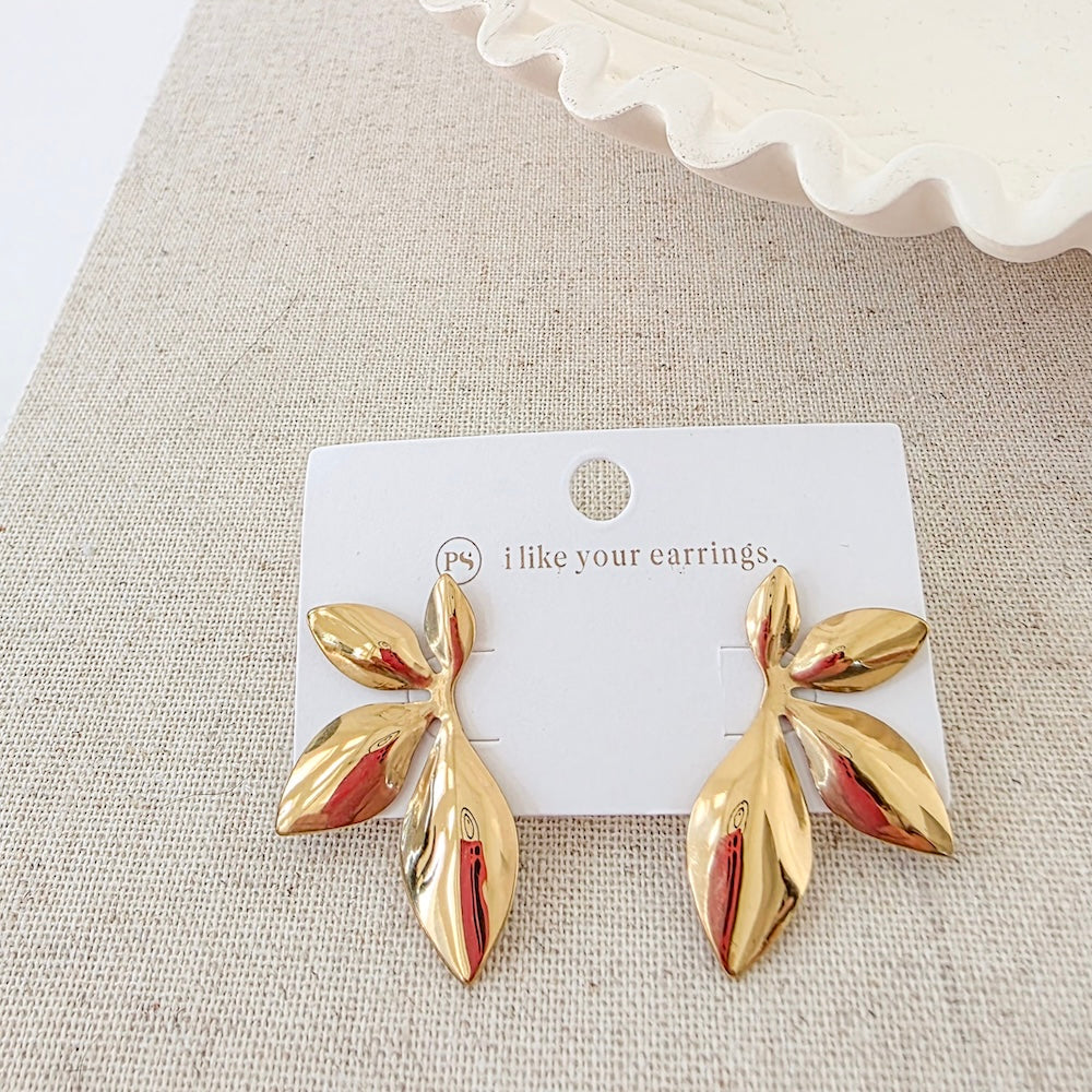 Pair of gold leaf drop earrings on a display card, with stud-style backings