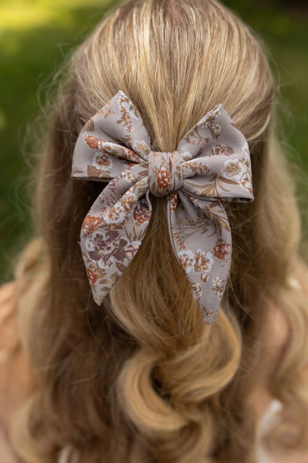 Floral hair bow in tan fabric with orange and brown flowers, tied on blonde hair