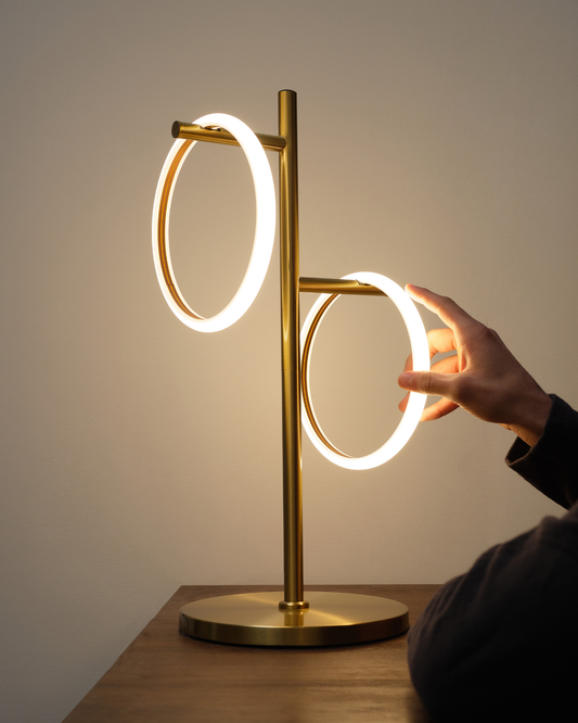 Gold and white Saturn table lamp with two glowing circular rings and round base.