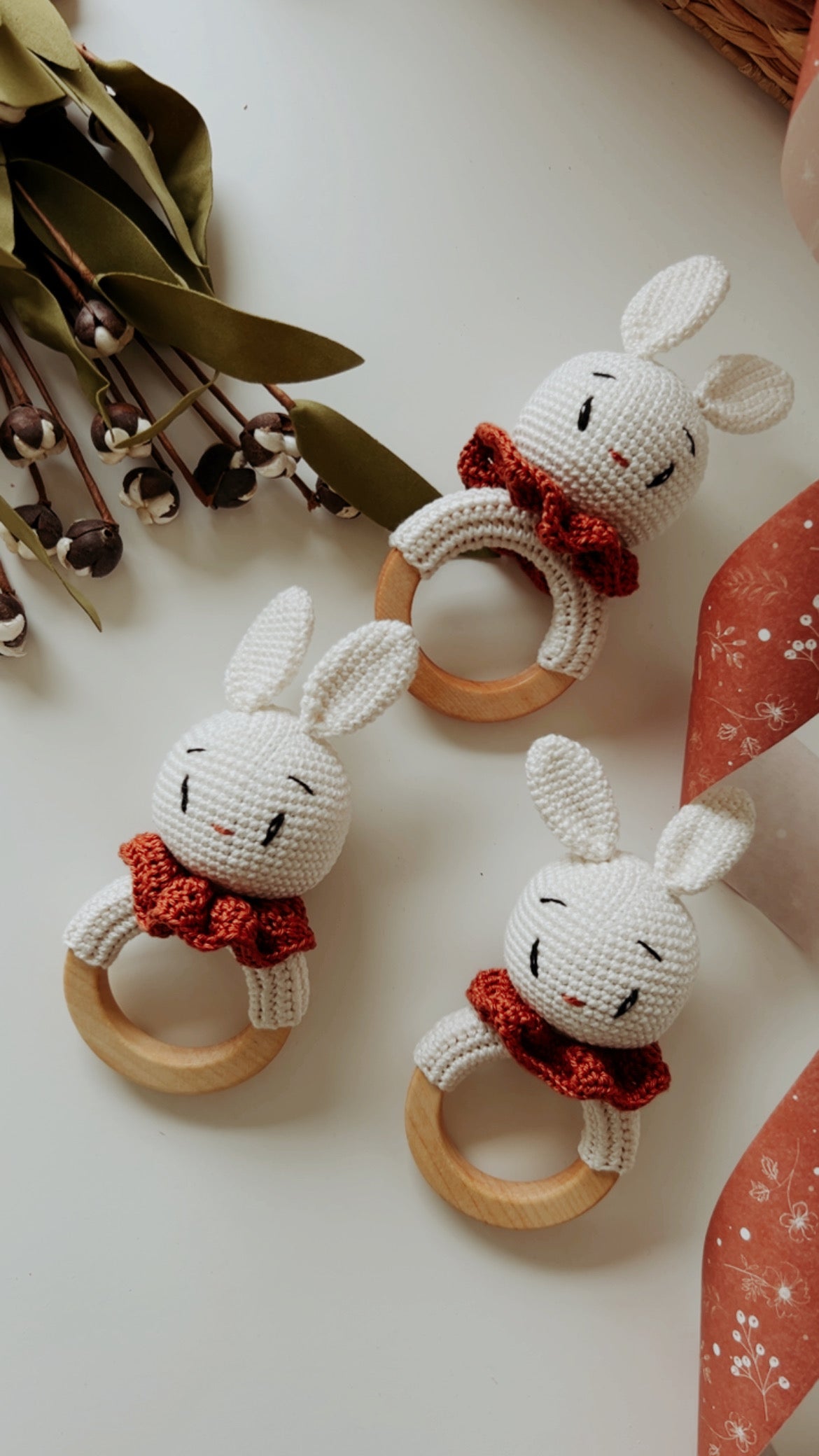 Three bunny rattle teethers: crocheted white bunnies with orange scarves and wooden rings