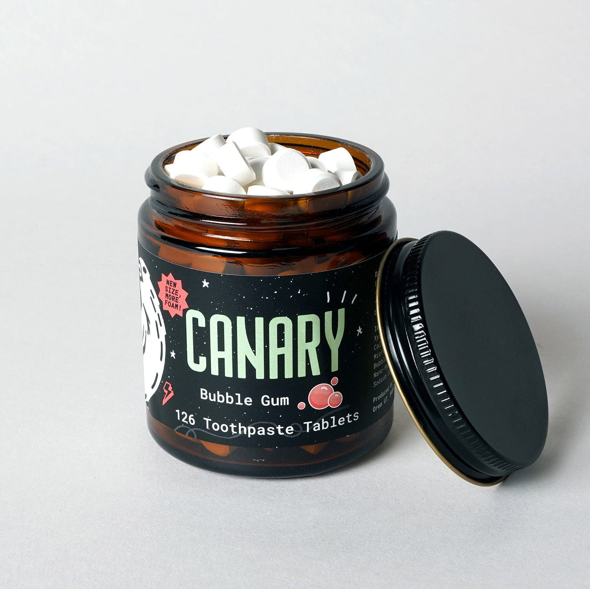 Open amber jar of CANARY toothpaste tablets, with white tablets and lid beside it