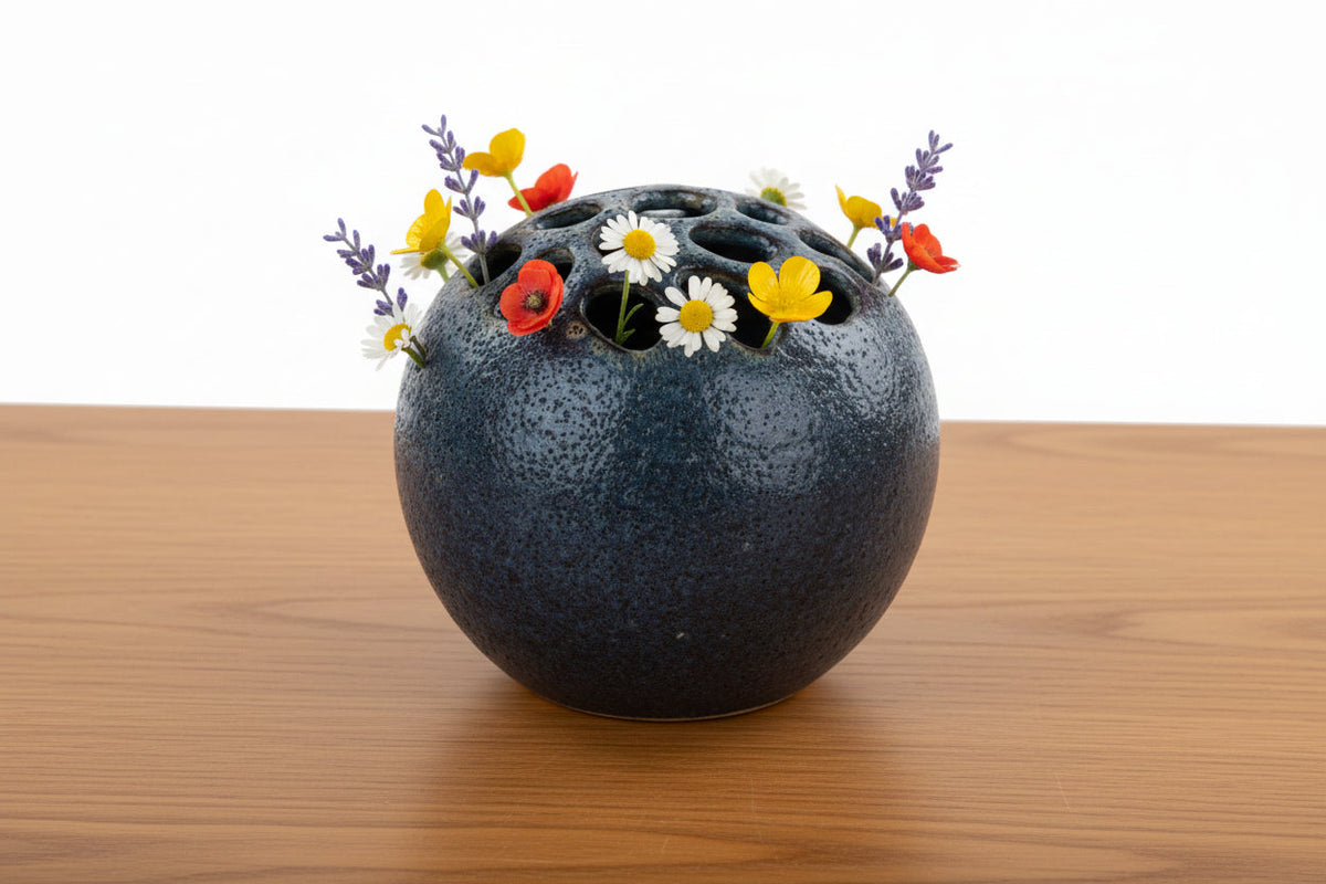 Blue-gray speckled ball vase with flowers arranged in punched hole top
