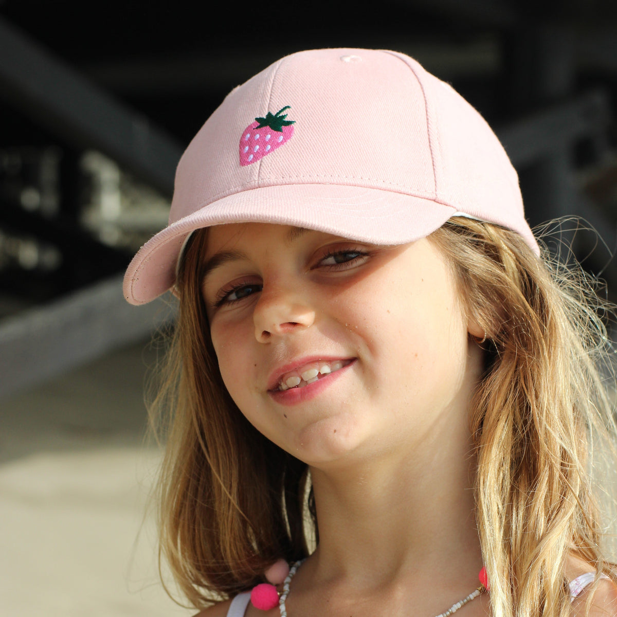Girl wearing a pastel pink baseball cap with a strawberry motif