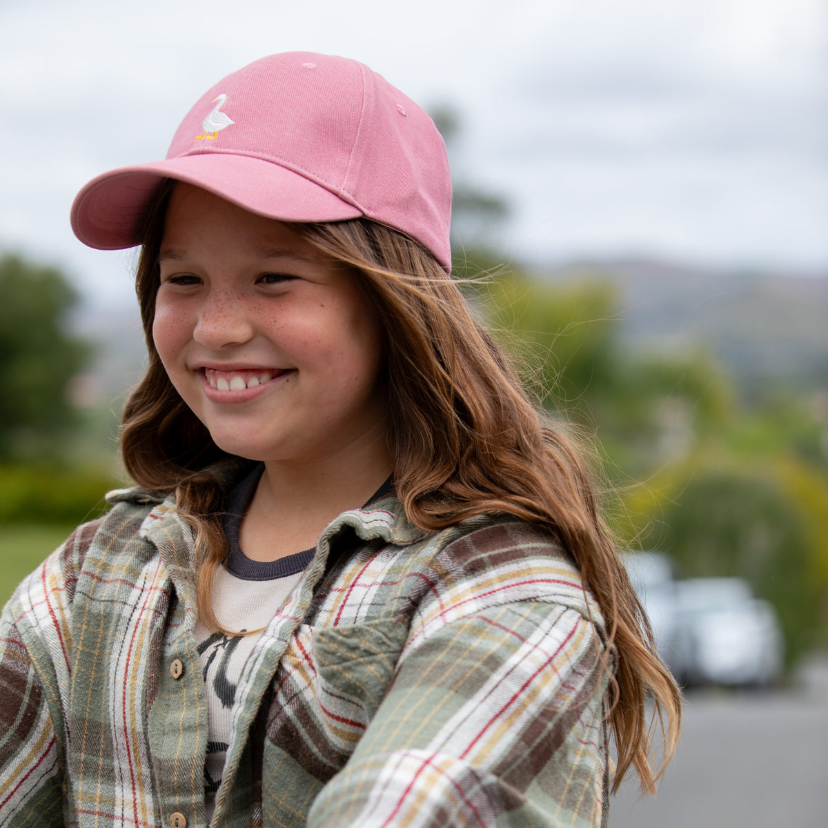 Kids mauve pink baseball cap with embroidered goose, worn by smiling child outdoors