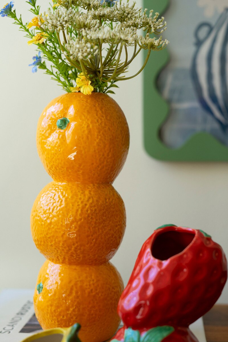 Stacked orange ceramic bud vase with flowers; red strawberry-style vase beside it