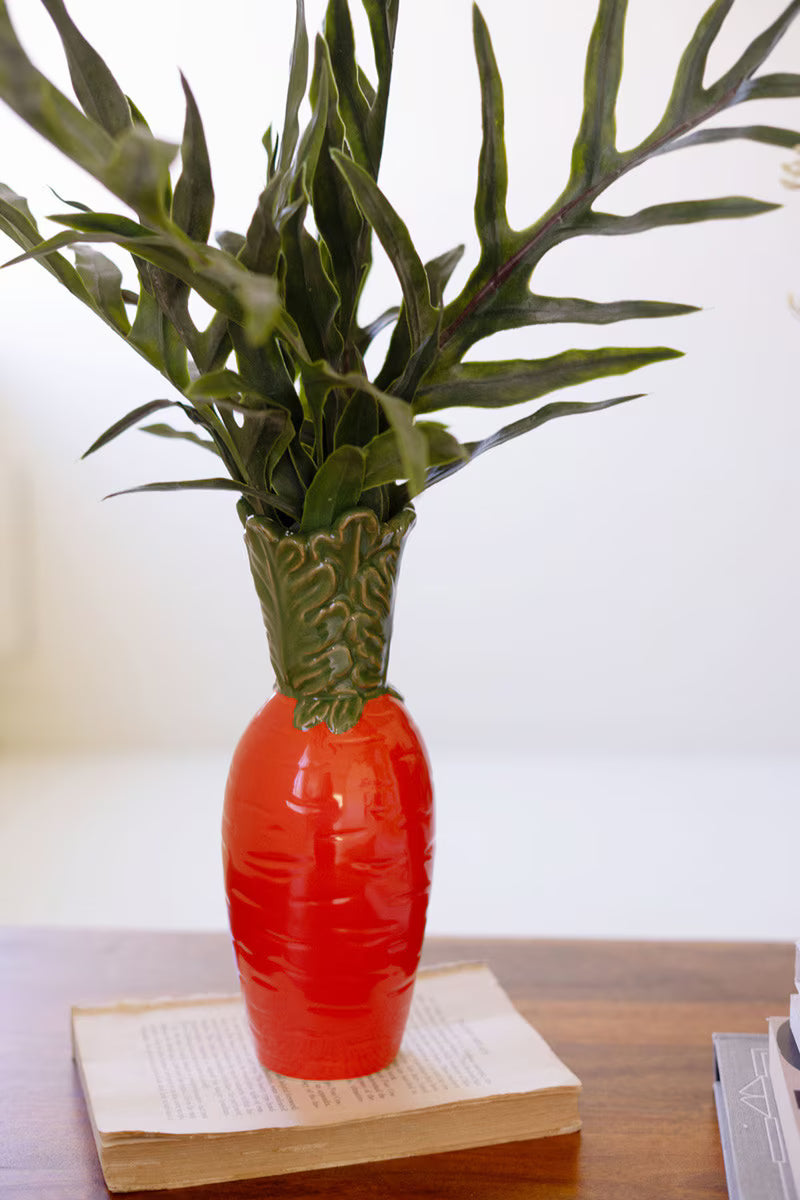 Orange ceramic carrot vase with green leafy top and smooth ridged body
