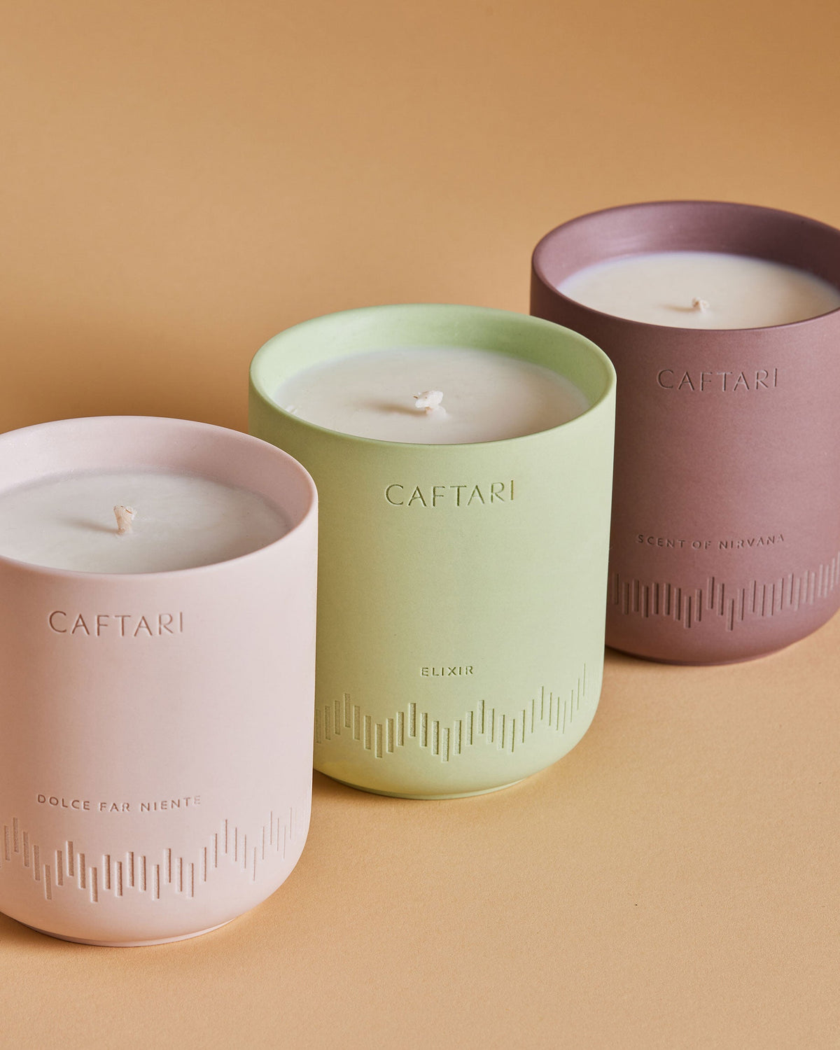 Caftari candles in pink, sage, and plum cups on a light surface