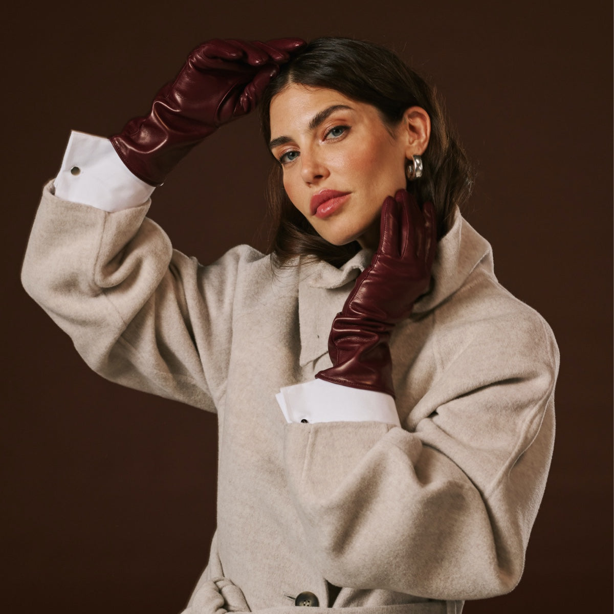 Model wearing long burgundy leather gloves with cashmere-lined cuffs and fitted fingers.