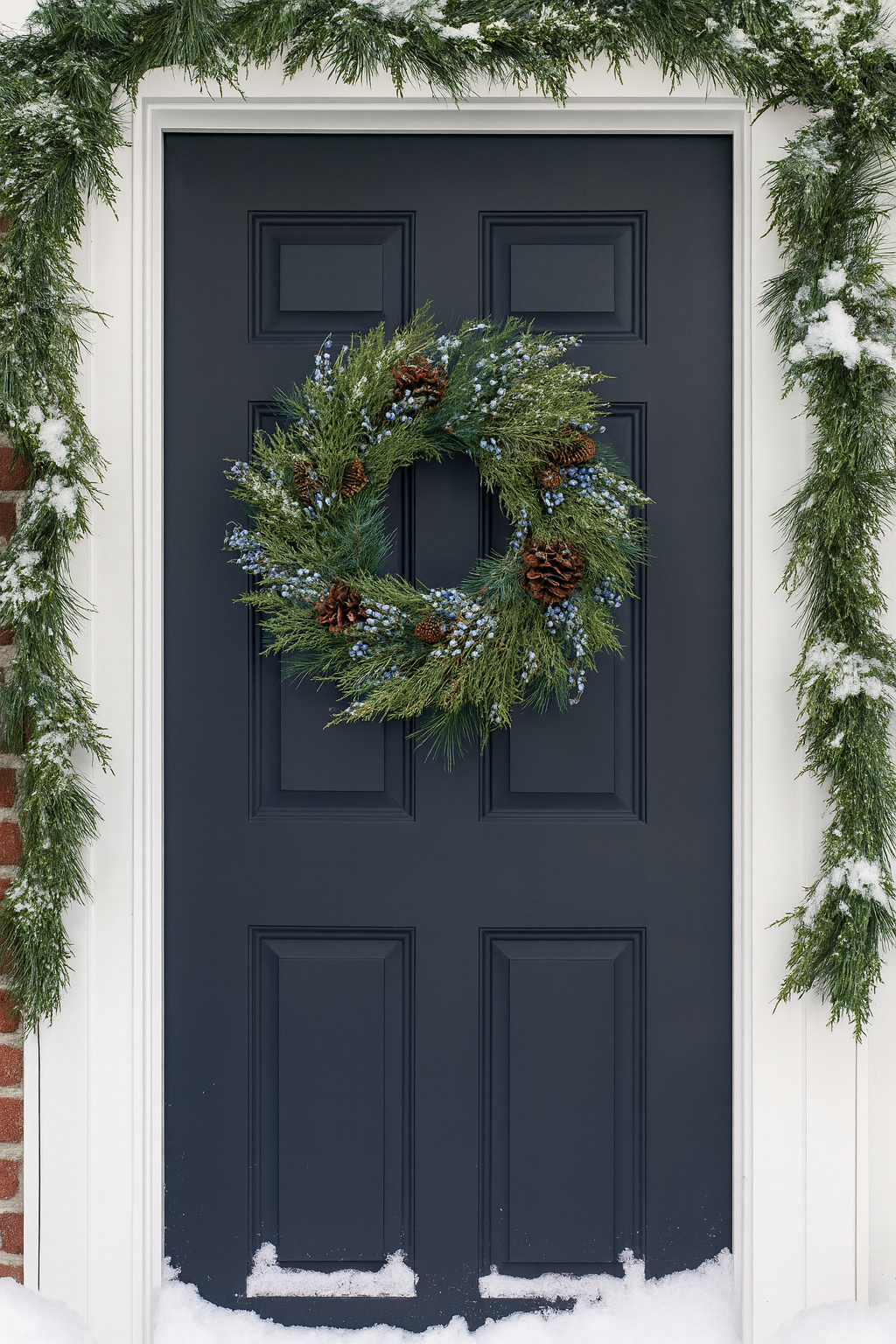 Evergreen wreath with blue berries and pinecones hanging on a front door