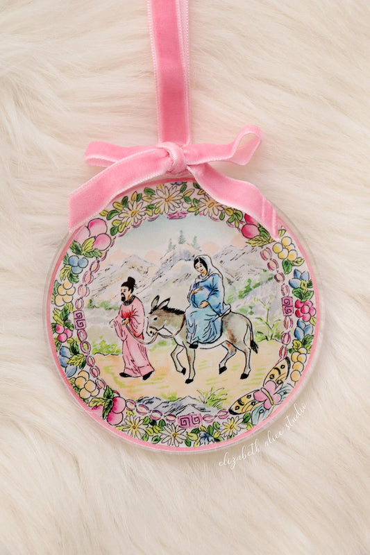 Round acrylic Christmas ornament with pink velvet bow and floral-bordered Bethlehem journey scene