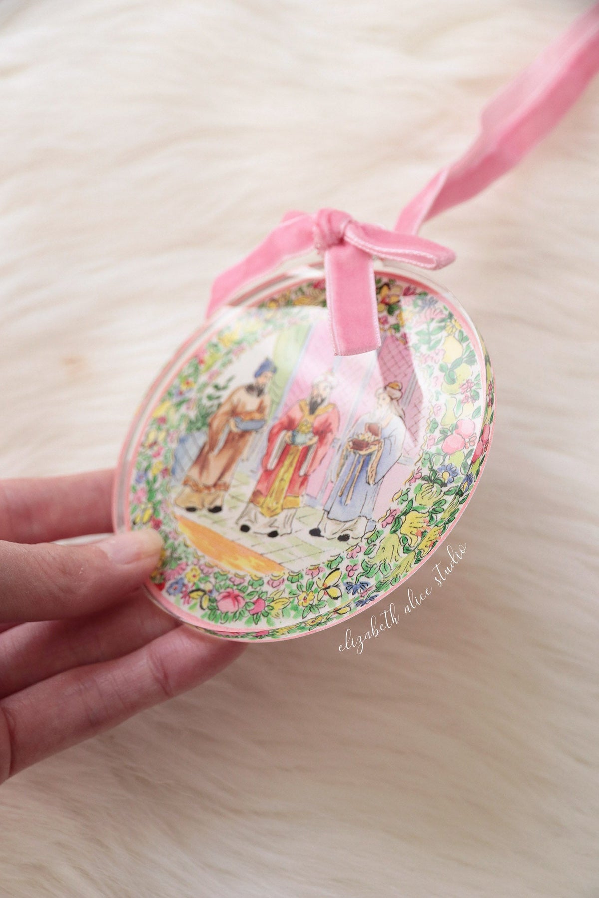 Angled view of round Magi ornament with floral border and pink bow