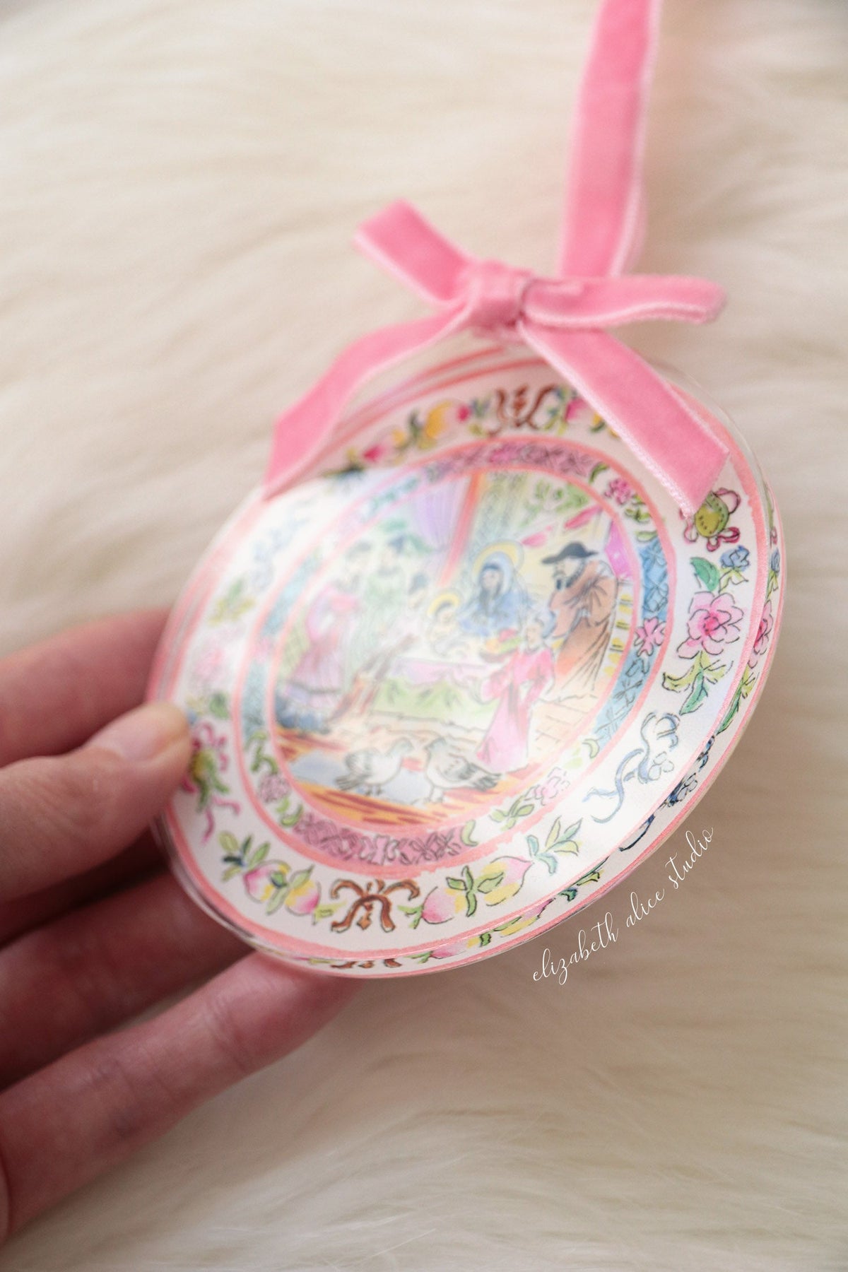 Close view of round acrylic ornament with pink velvet bow and floral border