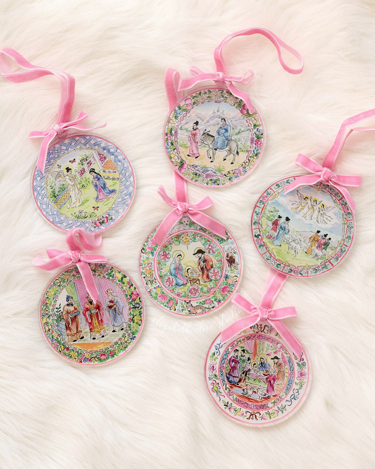 Five round acrylic Christmas ornaments with pink ribbon hangers and illustrated scenes