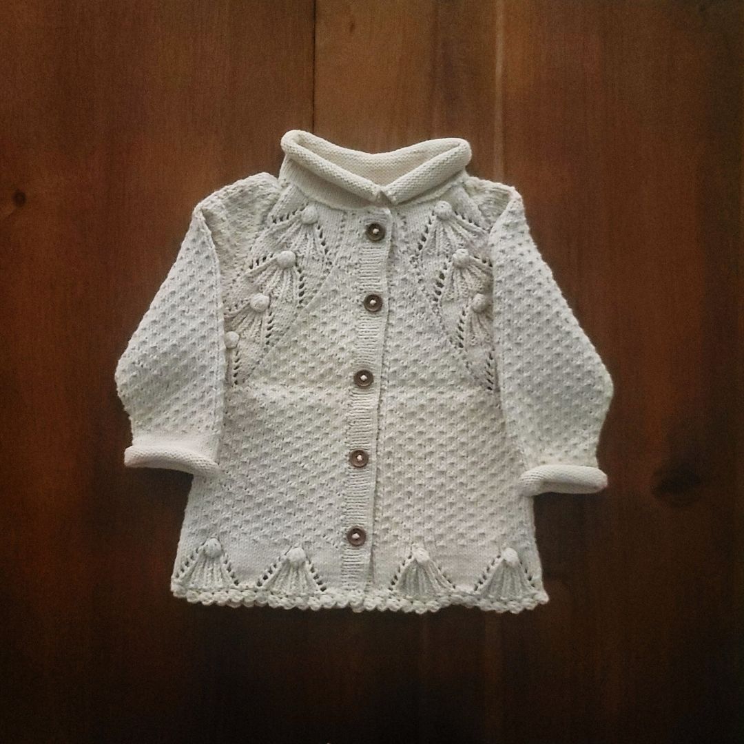 Ecru textured knit cardigan with snap buttons, long sleeves, and scalloped edges