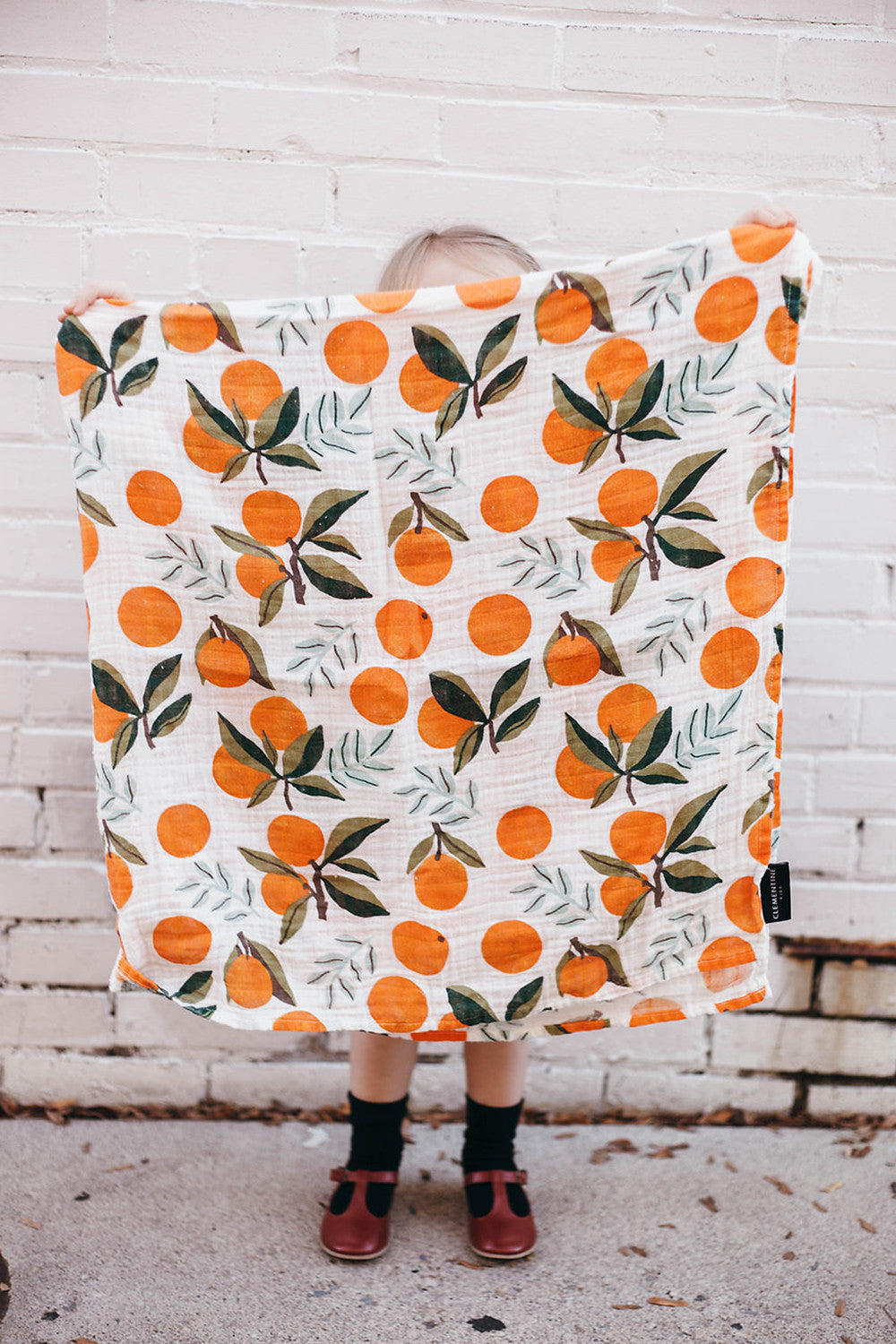 Swaddle blanket, white with orange fruit and green leaf pattern, folded square.