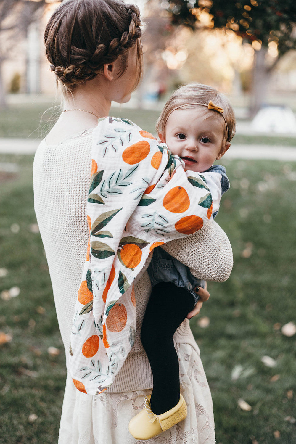 Baby swaddle blanket with orange fruit and green leaf print, draped over toddler.