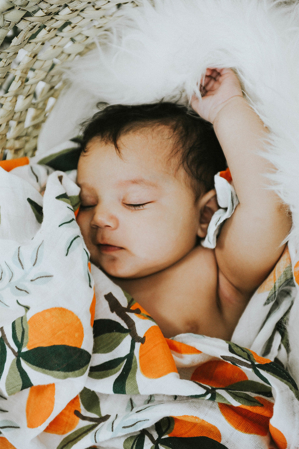 Swaddle blanket on sleeping baby, white with orange fruit and green leaf print.