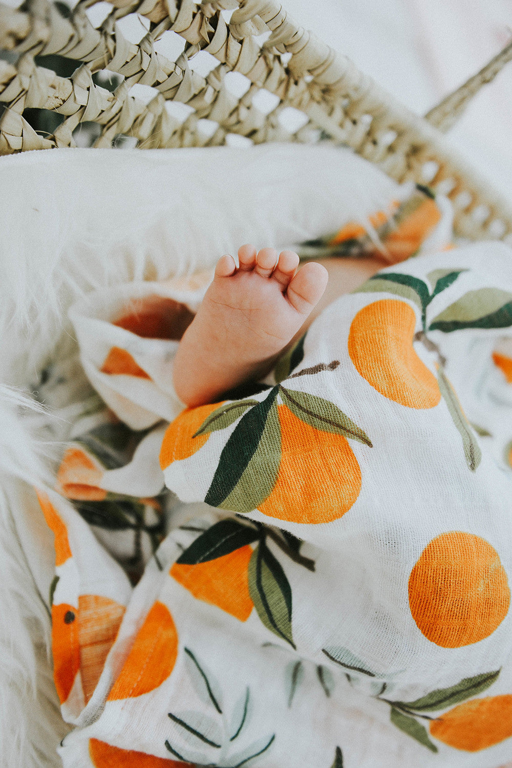 Swaddle fabric detail: white with orange fruit and green leaf print, soft weave.