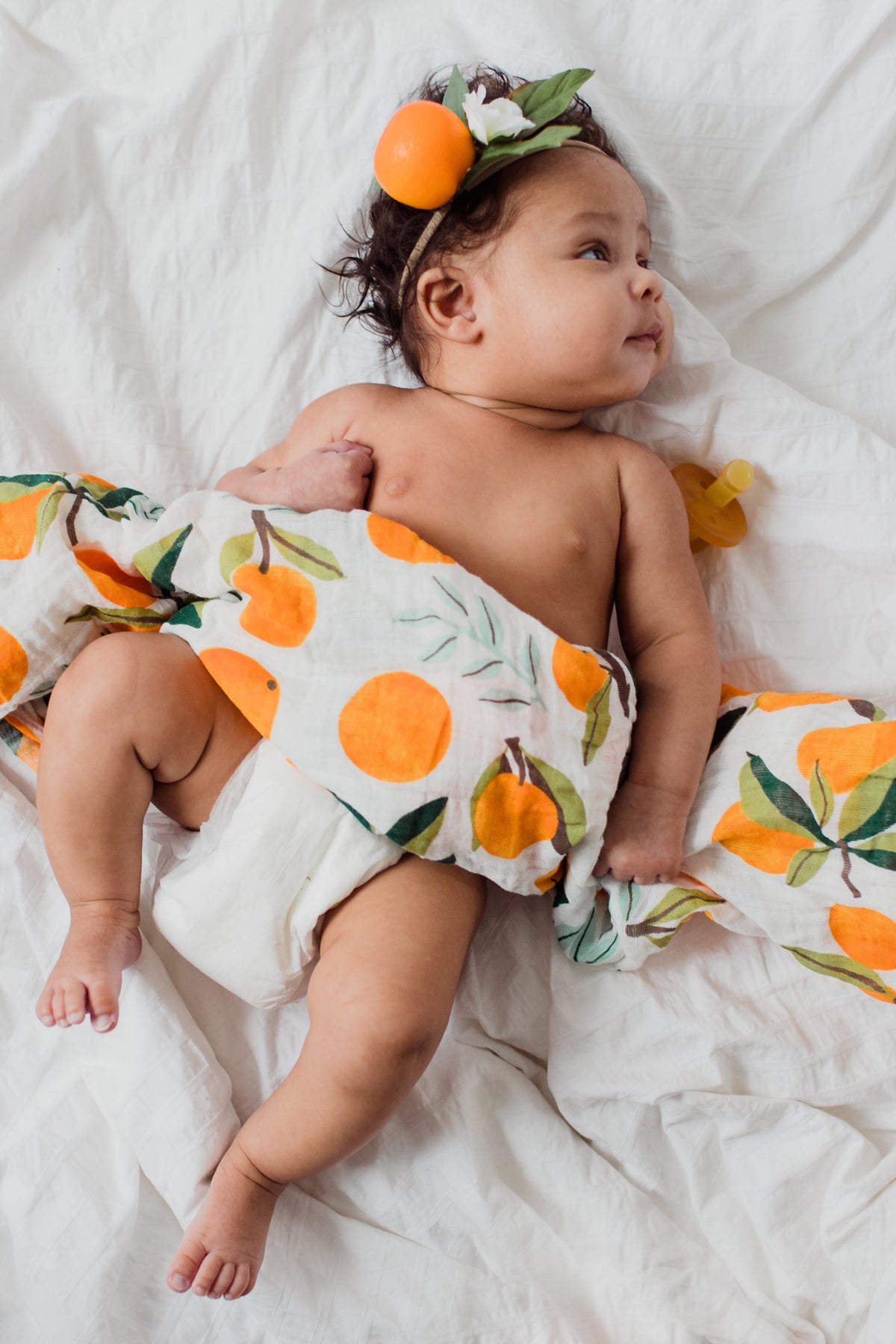 Baby swaddle blanket, white with orange fruit and green leaf pattern.