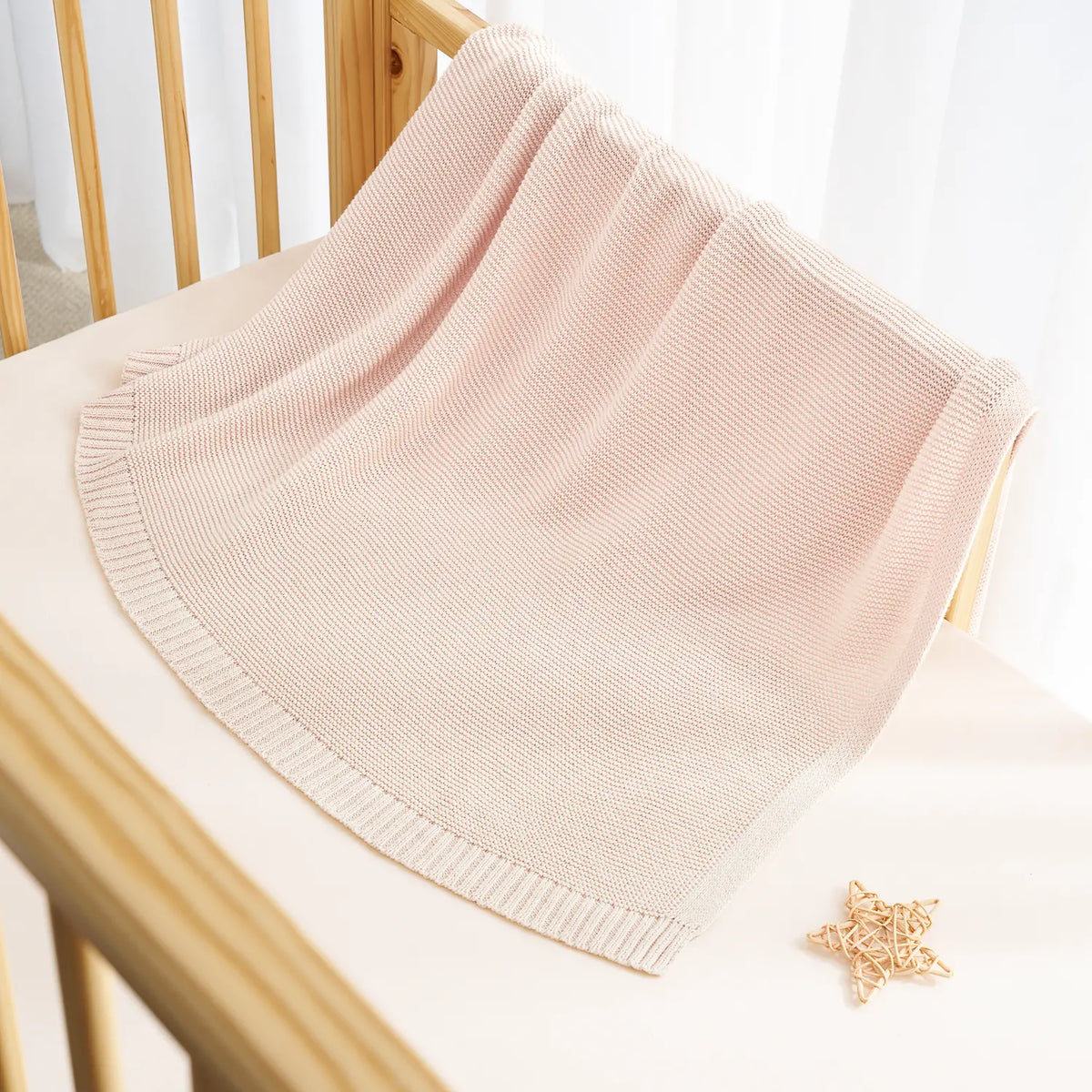 Beige knit cotton baby blanket draped with stitched ribbed hem and edging