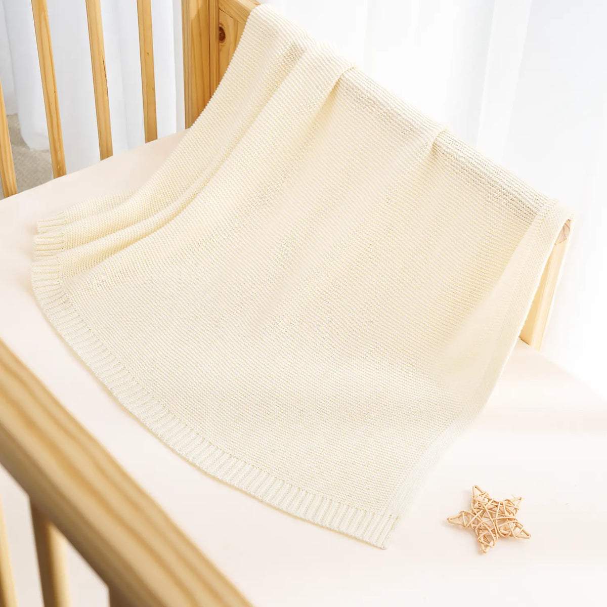 Cream knit baby blanket with ribbed edge and textured weave pattern.