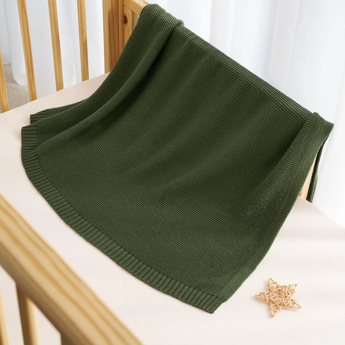 Forest green knit cotton baby blanket draped over a chair, ribbed edge