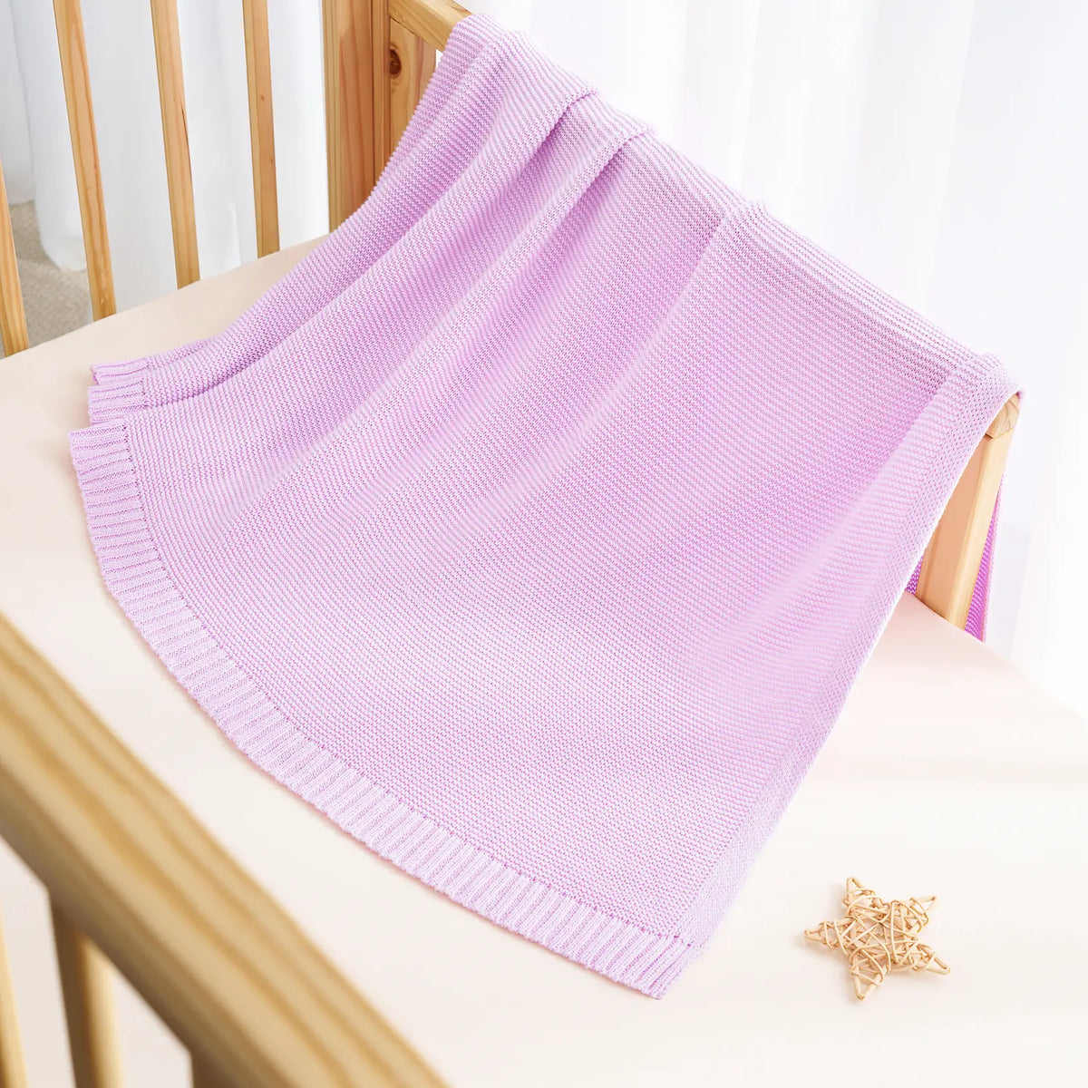 Lilac knit cotton baby blanket draped with ribbed hem border on a chair.