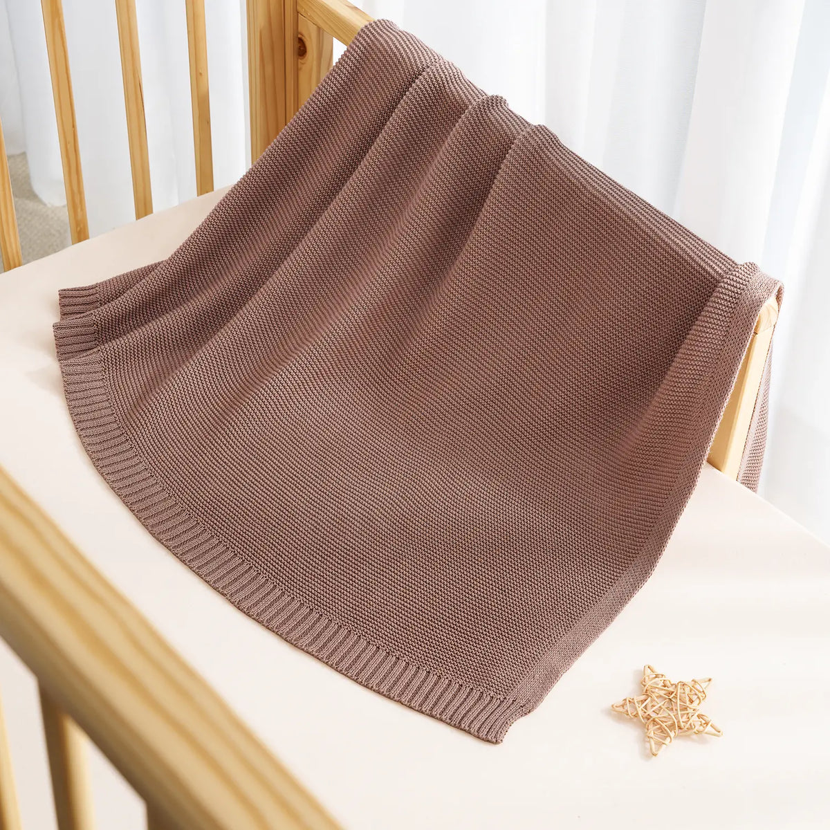 Mocha knit cotton baby blanket draped over a bed with ribbed edge trim