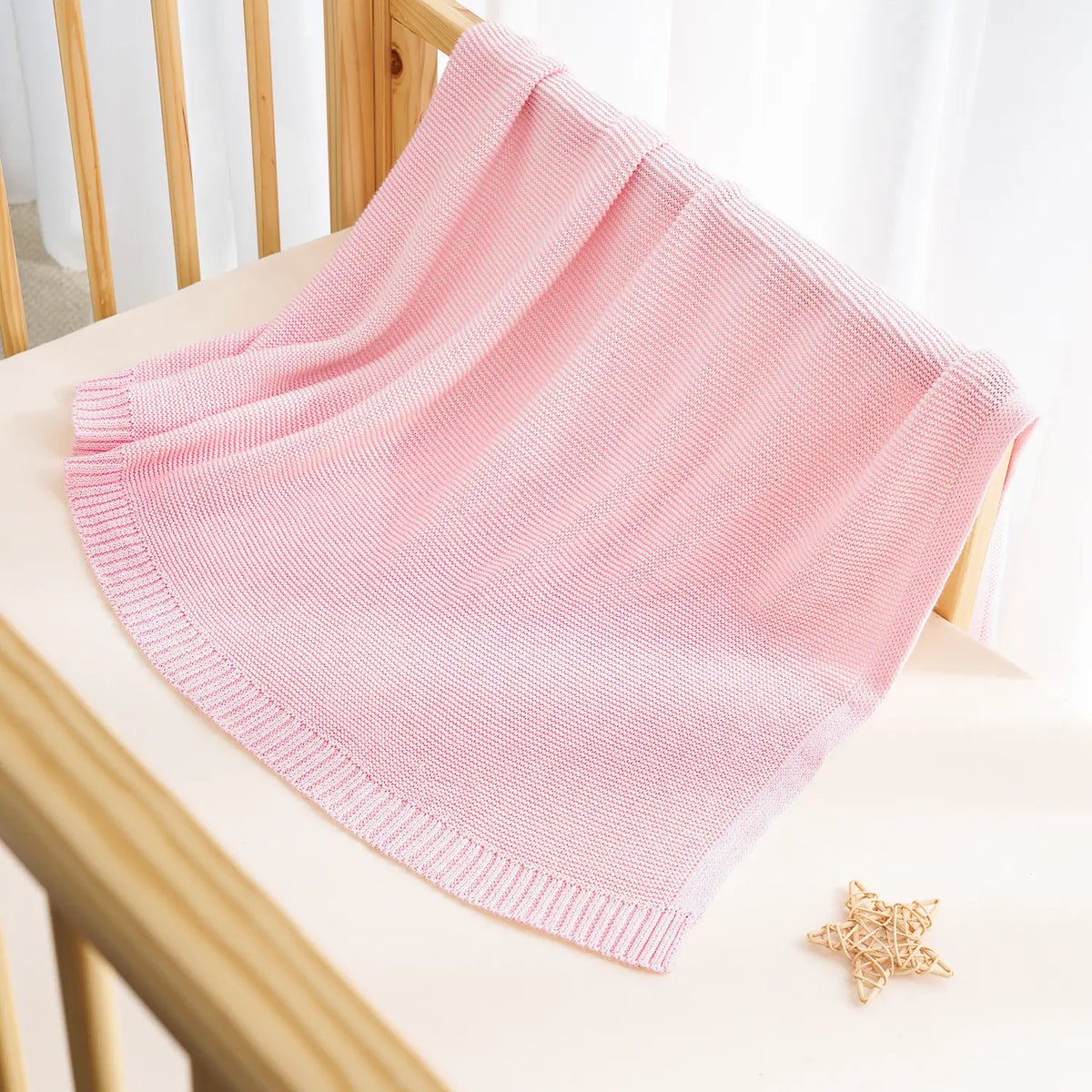 Pink knit cotton baby blanket draped with ribbed edge