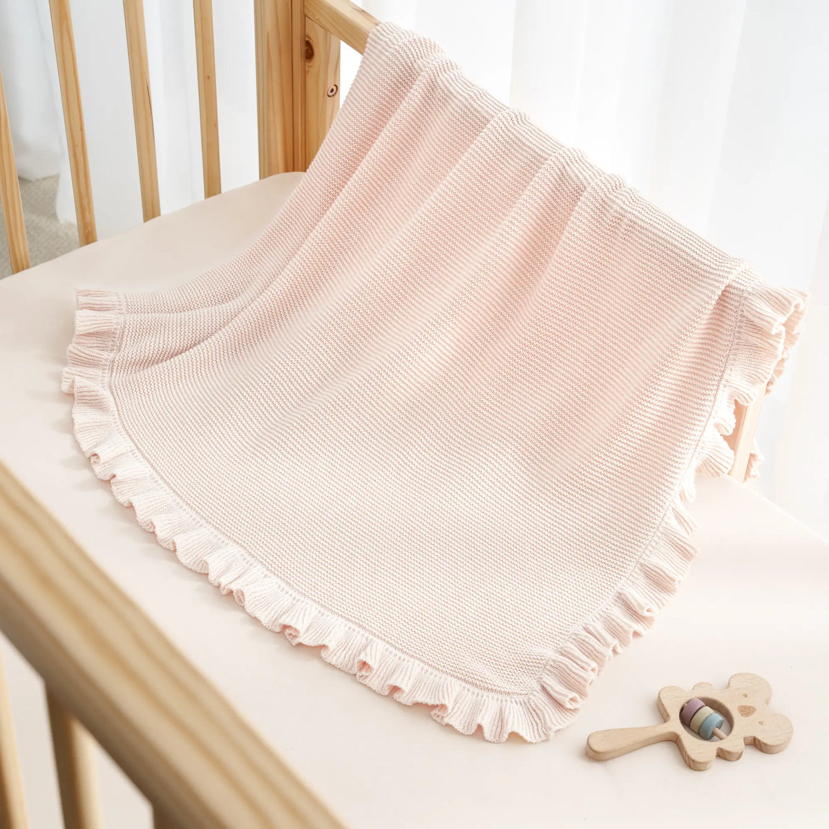 Beige knit baby blanket with ruffled trim draped on bed