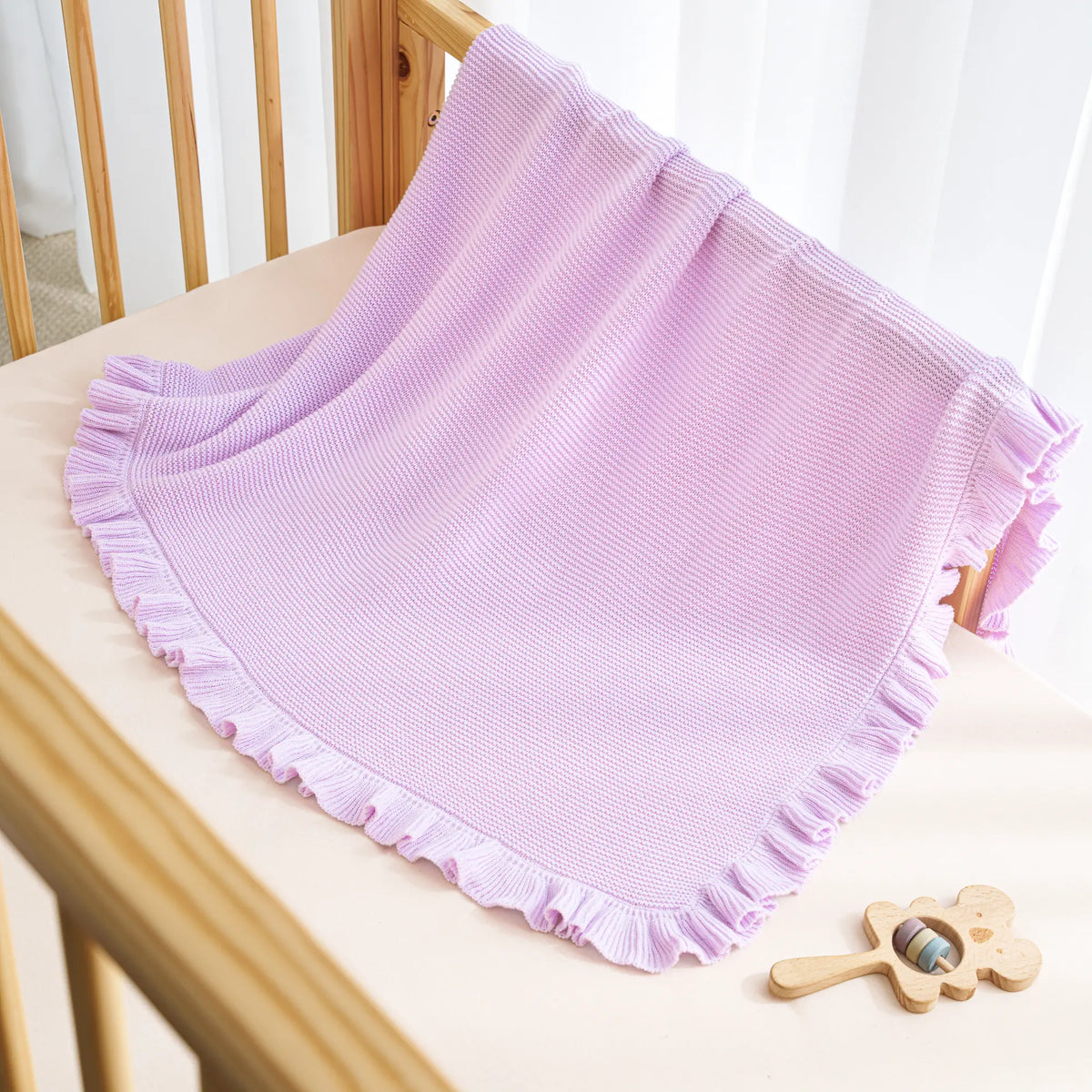 Lilac ruffled-edge knit baby blanket draped with gathered trim