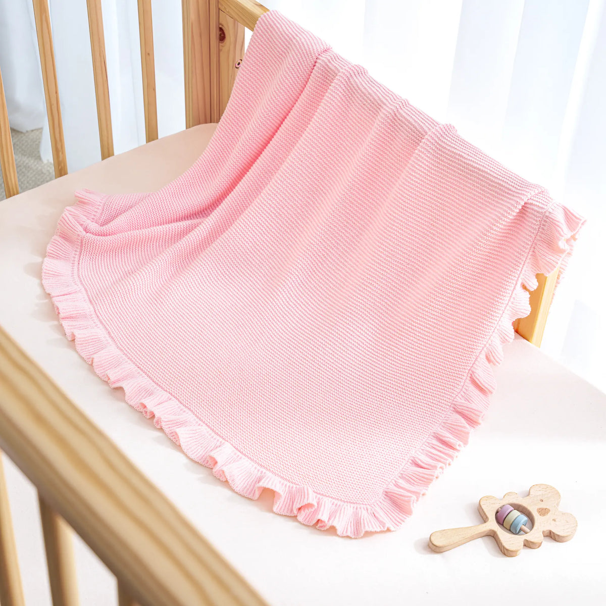 Pink ruffled-edge knit baby blanket draped over a chair