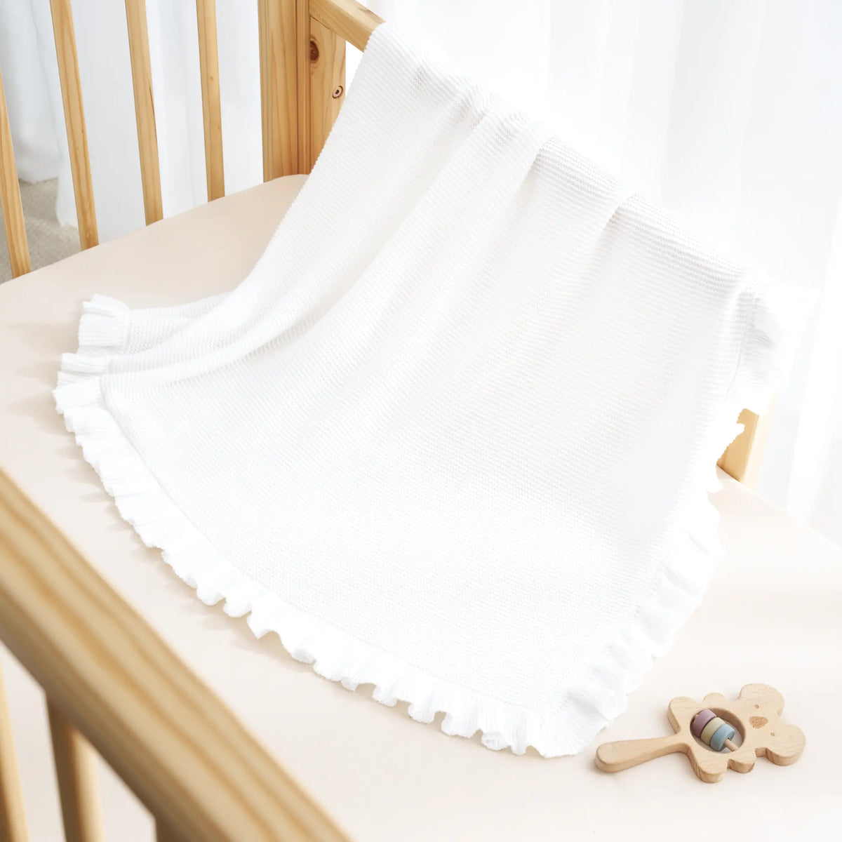 White knit baby blanket draped with ruffled edge trim