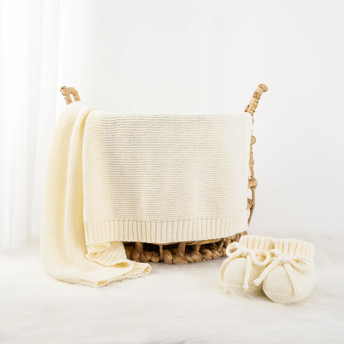 Cream knit baby blanket folded and draped on a cushion with knit tie accessories.