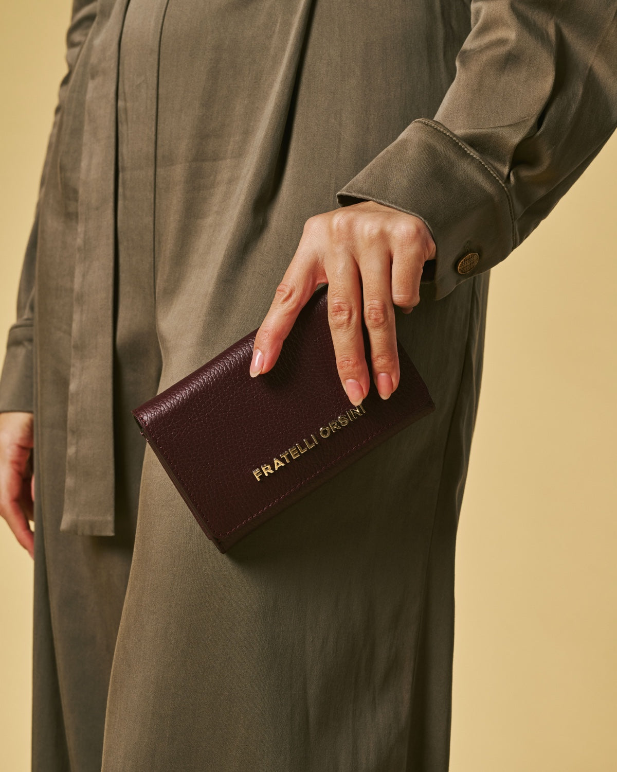 Eggplant purple leather women’s wallet with gold logo, held in hand
