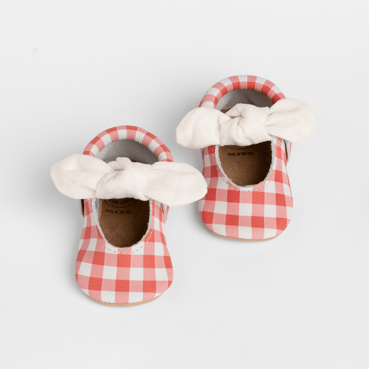 Gingham baby shoe with knotted white bow and red-and-white plaid fabric upper