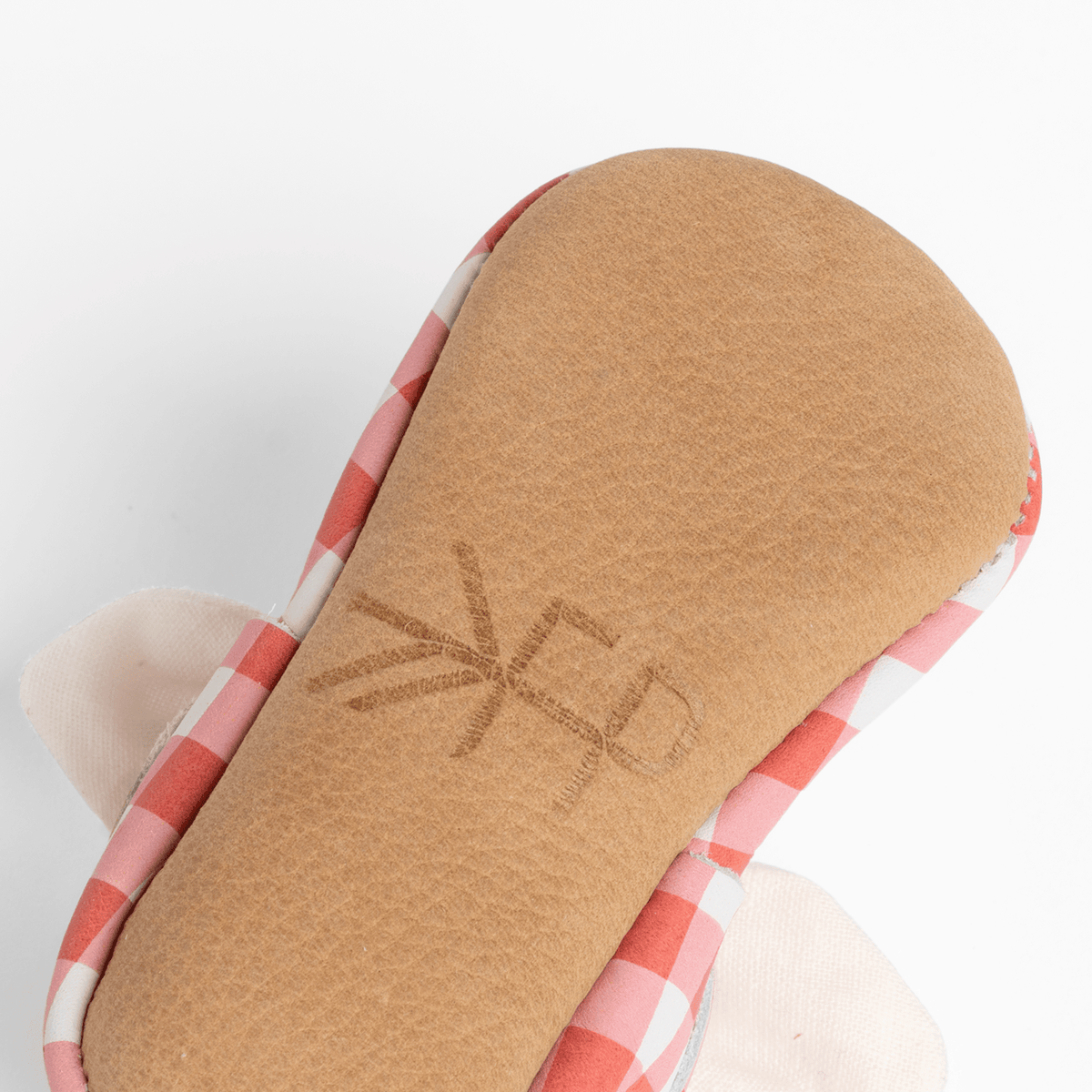 Close-up of red-and-white plaid baby shoe sole with textured tan underside
