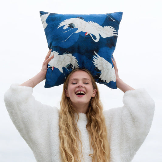 Blue crane-pattern throw pillow held above a person’s head